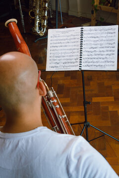 vertical image rear view of bald man studying and playing bassoon at home.