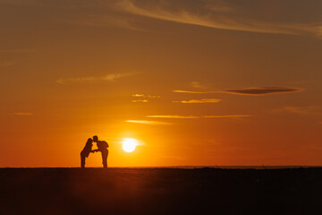 Fototapeta na wymiar silhouette of couple at sunset, woman and man holding hands walking along seashore in rays of sunset sunlight. walk and hug. place for text, romantic relationships, freedom and carelessness