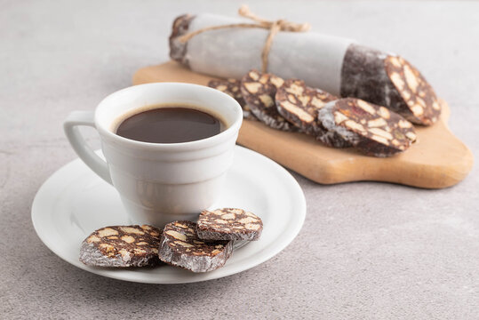 On a gray table is a blurry image of a cup of coffee and a chocolate salami in the background.