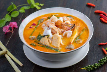 Tom Yam Kung or Tom Yum soup is Thai hot spicy soup shrimp or prawn with lemon grass, lemon, galangal, mushrooms, coconut milk and chili in bowl on wooden table top view, famous Thai food cuisine.