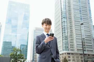 ビジネス街でスマートフォンを持つ20代から30代の笑顔のスーツ姿の男性