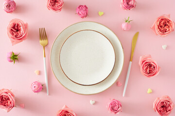 Flat lay composition of empty plate cutlery knife fork natural flowers pink peony rose buds and small hearts on isolated light pink background with blank space. Mother's Day concept