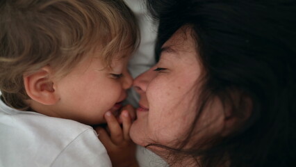 Mother and child love and care laying in bed. Lifestyle moment of mom and son eskimo kiss during...
