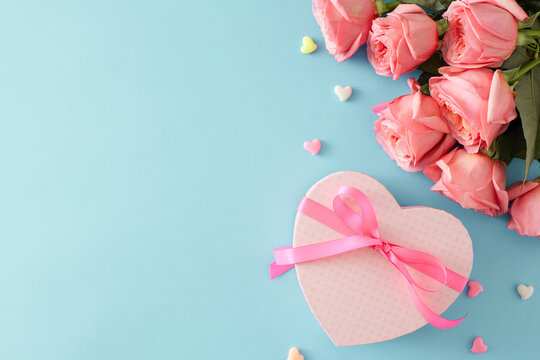 Mother's Day gift concept. Top view photo of heart shaped gift box with bow bunch of pink roses and small hearts baubles on isolated pastel blue background with empty space