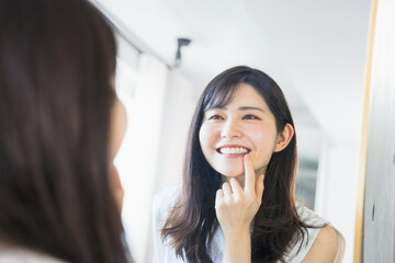 姿鏡の前で鏡に映る自分の歯の調子を眺めて笑顔になる20代〜30代の女性