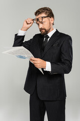 shocked businessman adjusting glasses and reading newspaper isolated on grey.