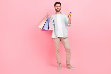 Full length photo of pretty cute man wear turquoise shirt rising shoppers chatting device isolated pink color background