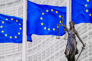 Themis and Europien Union flags on blurred buckground, shallow depth of field, focus on Themis statue. European Union law and jurisprudence