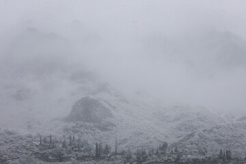Steep rocky mountain chain covered with fresh snow and covered by fog during a snowstorm