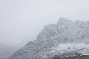 Steep rocky mountain chain covered with fresh snow and covered by fog during a snowstorm