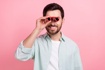 Photo of young smiling satisfied businessman spectator hold old antique watching opera antique binoculars isolated on pink color background