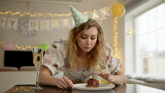 A woman hunching over the birthday cake and blowing a candle on it before taking a bite. She is visually sad about something. a High quality 4k footage