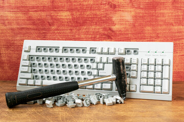 Broken computer keyboard and hammer on wooden background