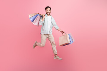 Full length photo of good mood cool man wear turquoise shirt jumping high rising shoppers isolated...