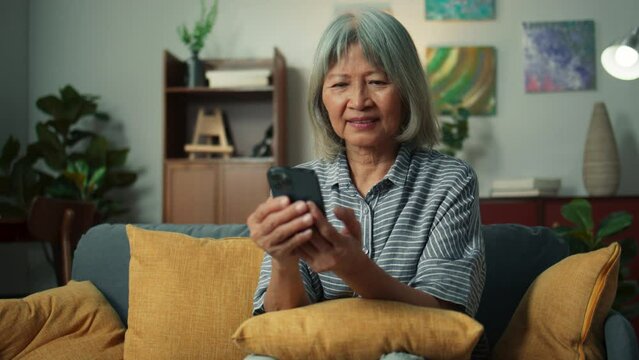 Closeup elderly woman hand using mobile phone technology application enjoy play social media checking email. Close up grandma holding smartphone scrolling looking at screen sit on sofa in living room