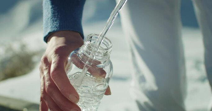 Close Up shot of Female Filling a Glass Bottle with Fresh Pure Cold Water from Natural Spring while Hiking