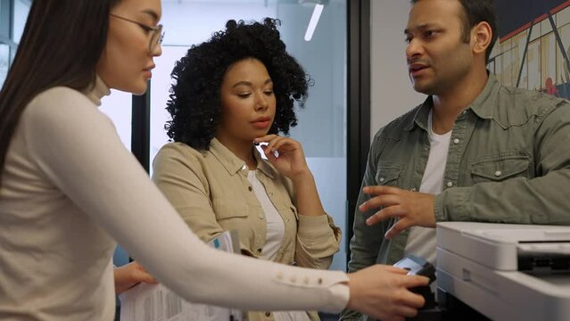 Confident multinational colleagues print documents on printer and talk in office