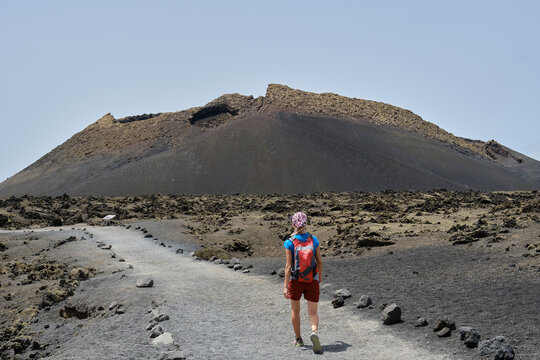 Woman with red backpack walking towards El Cuervo volcano in Lanzarote. Hiking in Lanzarote. Canary Islands