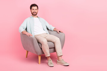 Full length photo of pretty cute man wear turquoise shirt sitting armchair empty space isolated pink color background
