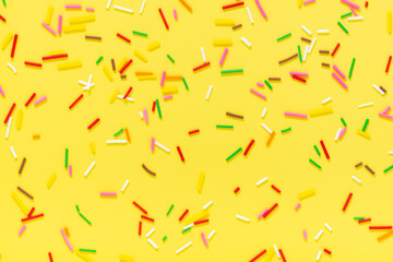flat lay of colorful sprinkles over yellow background, festive decoration for banner, poster, flyer, card, postcard, cover, brochure, designers
