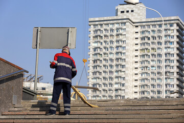 Man janitor in orange uniform sweeping the stone stairs on building background. Cleaning spring city