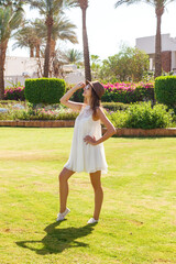 Woman on a holiday with sunglasses and white dress relaxing outdoor on a beautiful green park with palm trees