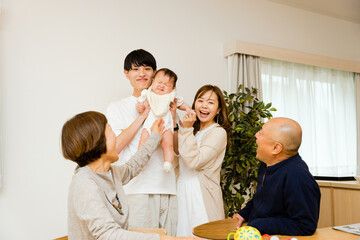 泣く赤ちゃんを抱っこする父親と母親とそれを見守る祖父母の5人の家族