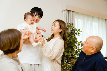 泣く赤ちゃんを抱っこする父親とあやす母親とそれを見守る祖父母の5人家族