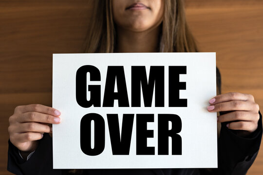 Game over. Woman holds a white page with text "Game Over" in black letters. Information sign, leisure games, finishing, end, strategy and video game.