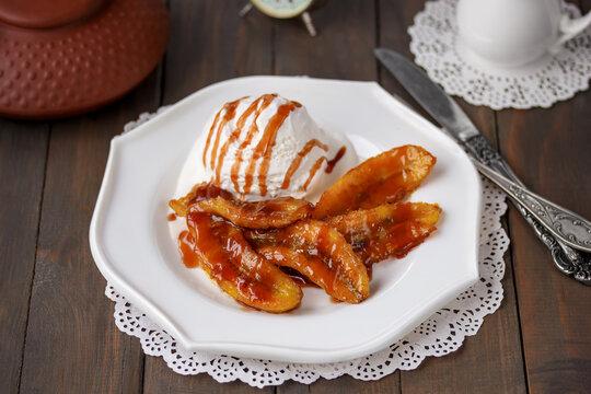 Bananas Flambe or Bananas Foster. A portion of sweet caramelized sliced bananas and a flamb&eacute;ed rum sauce served with scoop of vanilla ice cream on white plate. Selective focus, horizontal