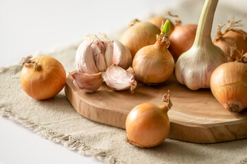Onions and garlic lie on the table on a wooden board and a canvas napkin.