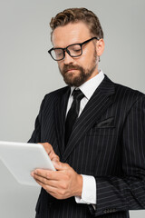 businessman in formal wear and glasses using digital tablet isolated on grey.