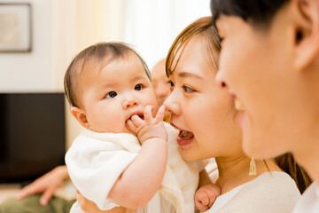 赤ちゃんを抱っこしてあやす20代〜30代の母親の女性と見守る父親