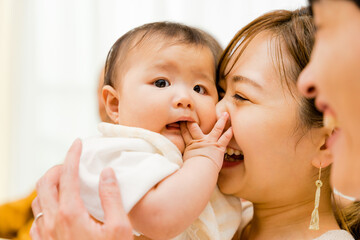 赤ちゃんを抱っこしてあやす20代〜30代の母親の女性と見守る父親