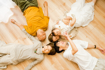 床に並んで上向きで寝そべる赤ちゃんと両親と祖父母の3世代の家族5人