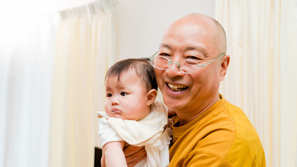 0歳の孫の赤ちゃんを抱っこする笑顔でカメラ目線のおじいちゃん