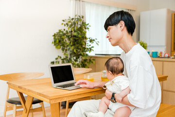 Obraz premium リビングで0歳児の赤ちゃんを抱っこしながら仕事をする父親の男性