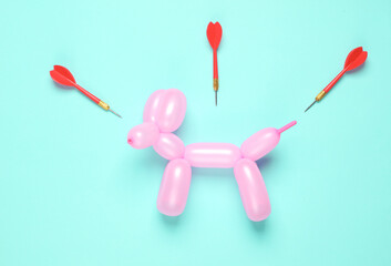 Pink balloon in the shape of dog and darts on a blue background. Top view