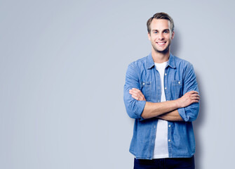 Portrait image - happy smiling handsome man standing in folded hands pose, isolated over grey gray background. Male model in blue casual cloth at studio.