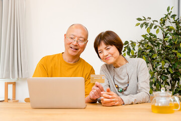 リビングで仲良くクレジットカードでネットショッピング決済をする笑顔の50代から60代のシニア夫婦