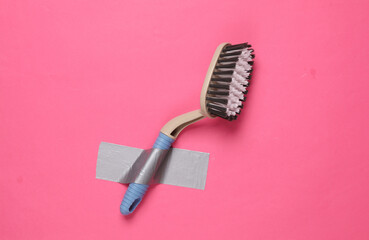 Cleaning brush fixed with adhesive tape on a pink background. Conceptual pop, contemporary art, minimalist still life