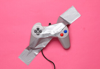 Retro gamepad fixed with adhesive tape on a pink background. Conceptual pop, video game
