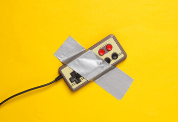 Retro gamepad fixed with adhesive tape on yellow background. Conceptual pop, video game