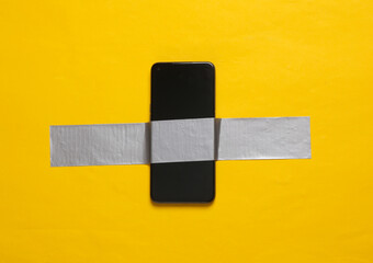 Smartphone fixed with adhesive tape on yellow background. Conceptual pop, contemporary art