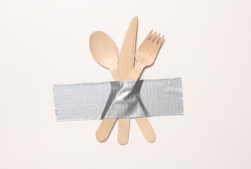Eco wooden spoon, fork and knife fixed with adhesive tape on white background. Conceptual pop, contemporary art. Food concept