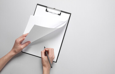 Female hand puts a signature on an empty sheet of paper in a clipboard, gray background