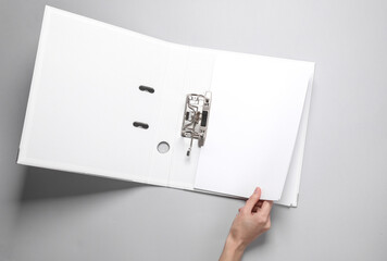 Female hand holds a sheet of paper open binder folder on a gray background. Template for design. Business concept