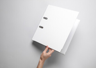 Female hand holding white binder folder on gray background