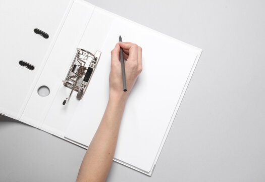 Female hand writes on a sheet of document in an open binder folder on gray background
