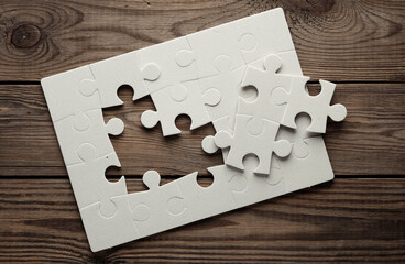 White jigsaw puzzle pieces on wooden background.